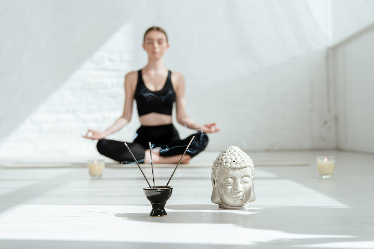 Human Design gates | A woman meditating against a white wall, with incense burning in the foreground.