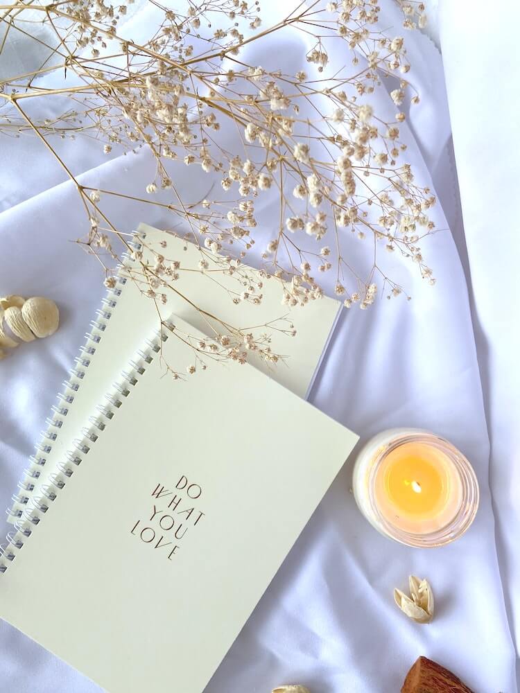 A notebook with the words 'do what you love' on the front, beside a candle and a sprig of baby breath.