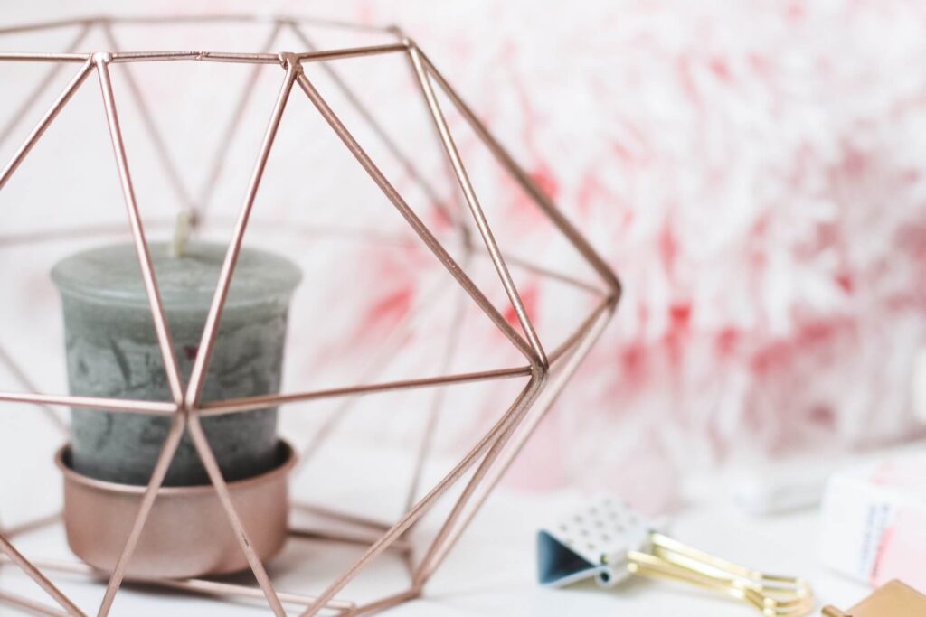 How to write a manifestation list | A candle inside a rose gold geometric cage, beside pink flowers and a bulldog clip.