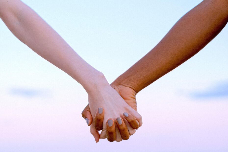 Human Design split definition | Two hands holding each other against the backdrop of a pink sky.