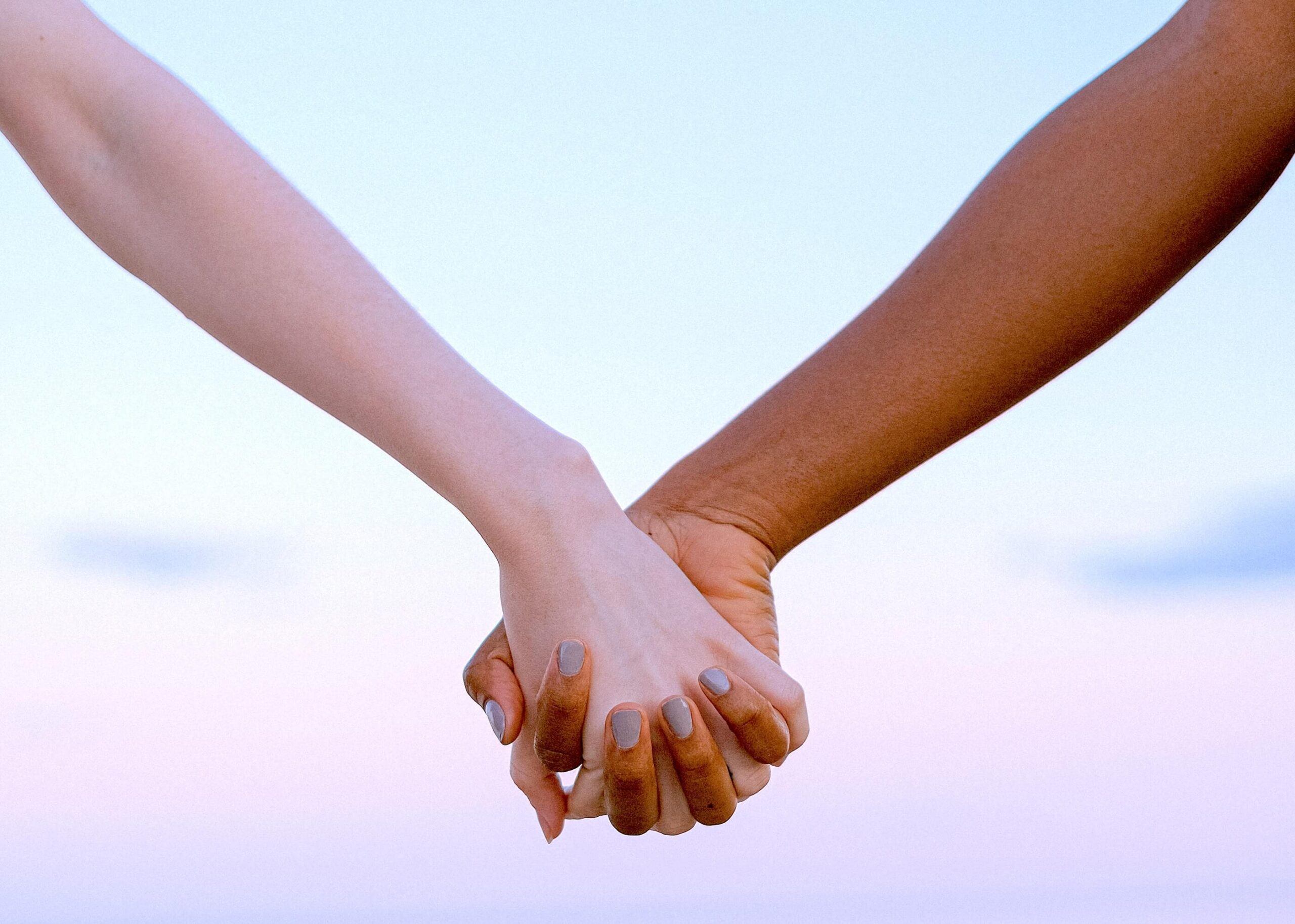 Human Design split definition | Two hands holding each other against the backdrop of a pink sky.