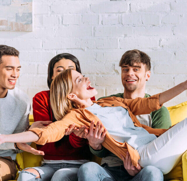 4/6 Human Design Profile - Opportunist Role Model.| A woman in an orange shirt and white t-shirt lays across three friends on a sofa.