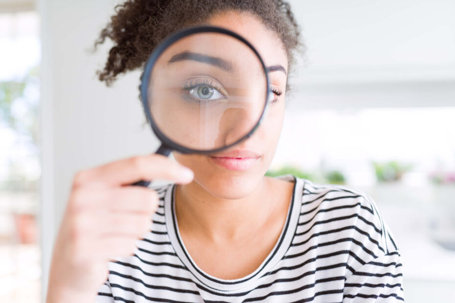 1/3 Human Design profile | A young woman with curly black hair peers through a magnifying glass. She wears a black and white stripy top.