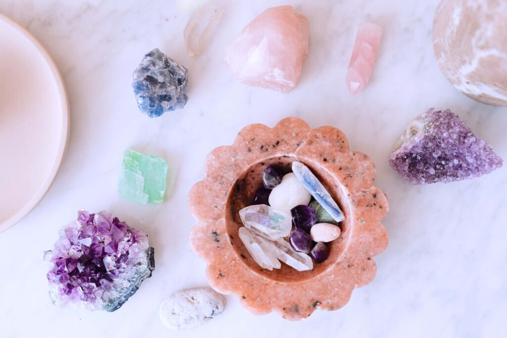 Feminine energy crystals | Flatlay of a selection of crystals on a marble surface and in an earthenware bowl, including rose quartz and amethyst.
